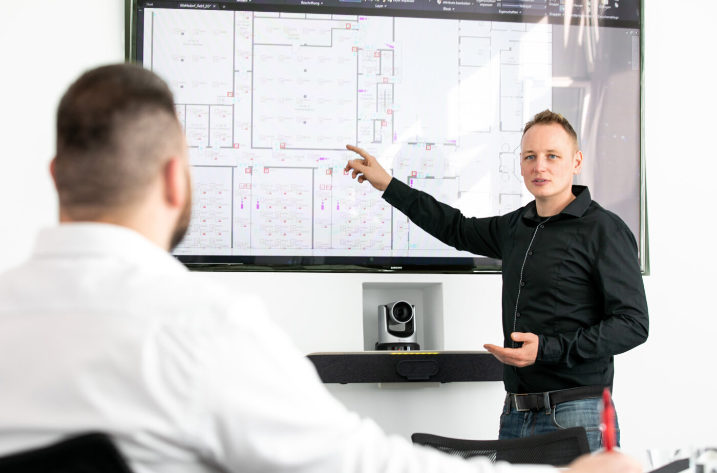 Ein Mitarbeiter der WTG Sicherheitssysteme erklärt einem anderen Mitarbeiter etwas an einem Whiteboard.