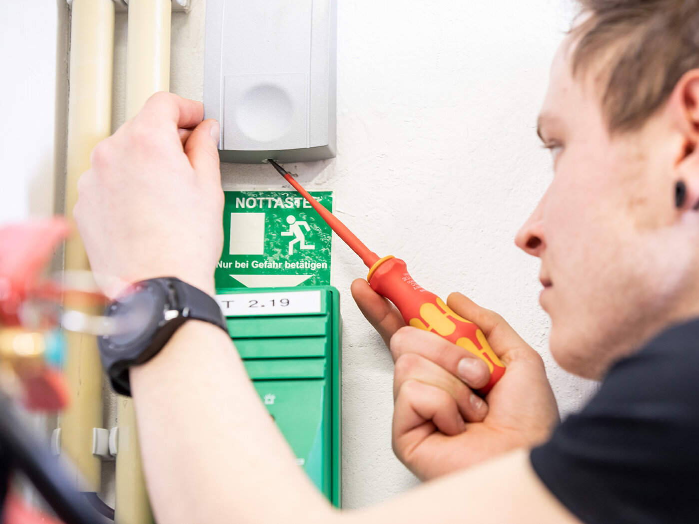 Ein Mitarbeiter der WTG Sicherheitssysteme schreibt mit einem Schraubenzieher an einem Kasten für Fluchttürsicherung.