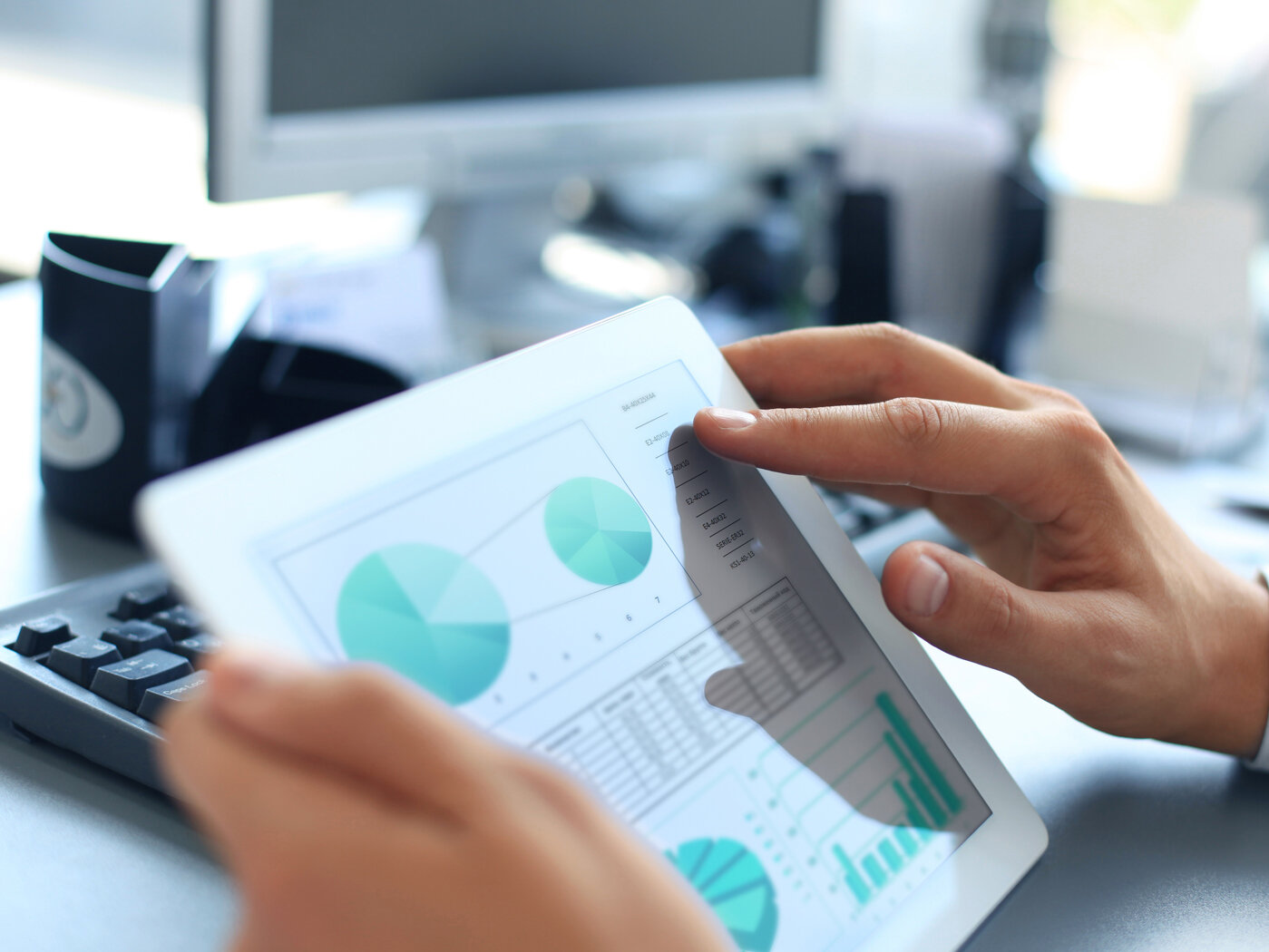 Eine Person, von der nur die Hände zu sehen sind, studiert Kuchendiagramme auf einem Tablet.