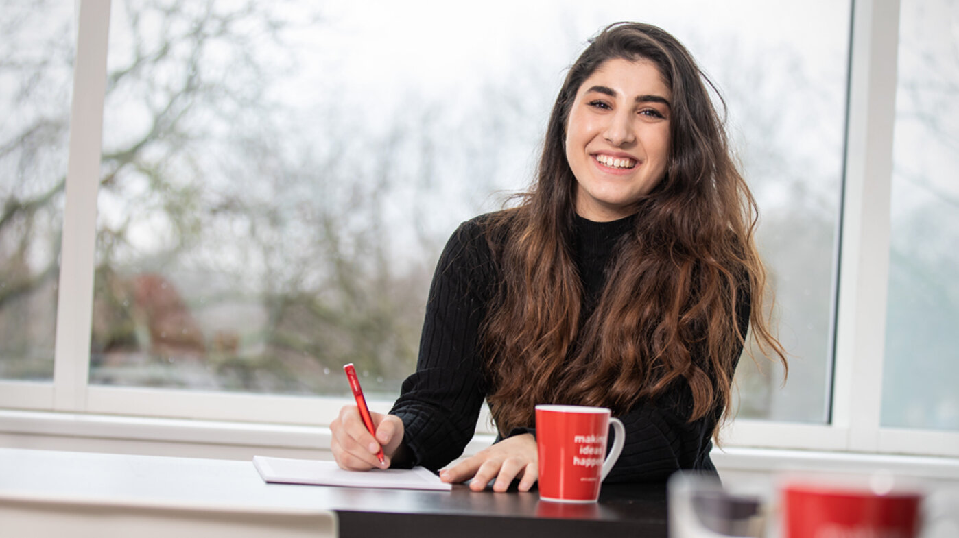 Eine Mitarbeiterin sieht von ihren Notizen auf und lächelt in die Kamera