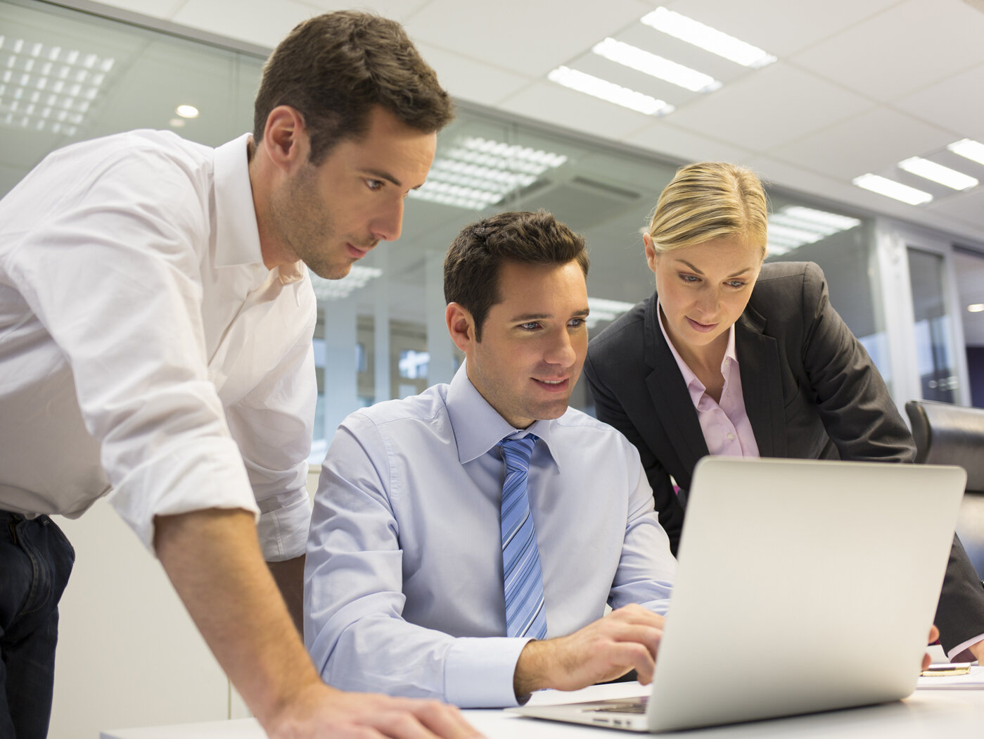 Zwei Männer und eine Frau blicken auf den Bildschirm eines Laptops.
