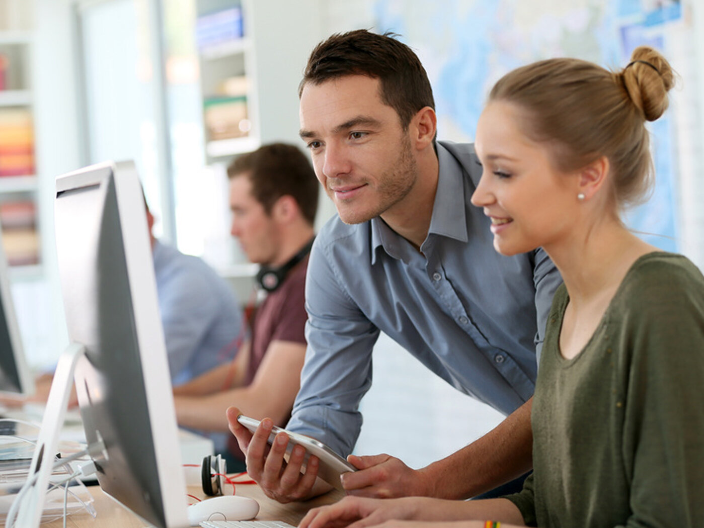 Eine Frau sitzt vor einem Rechner, während sich ein Mann dazubeugt.