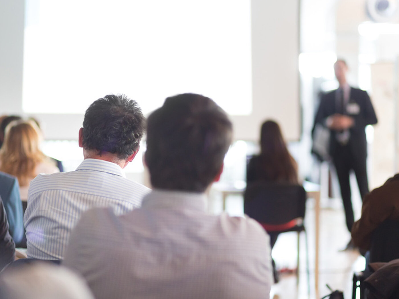 Eine Gruppe von Menschen nimmt an einer Schulung teil und blickt auf den Sprecher im Hintergrund.