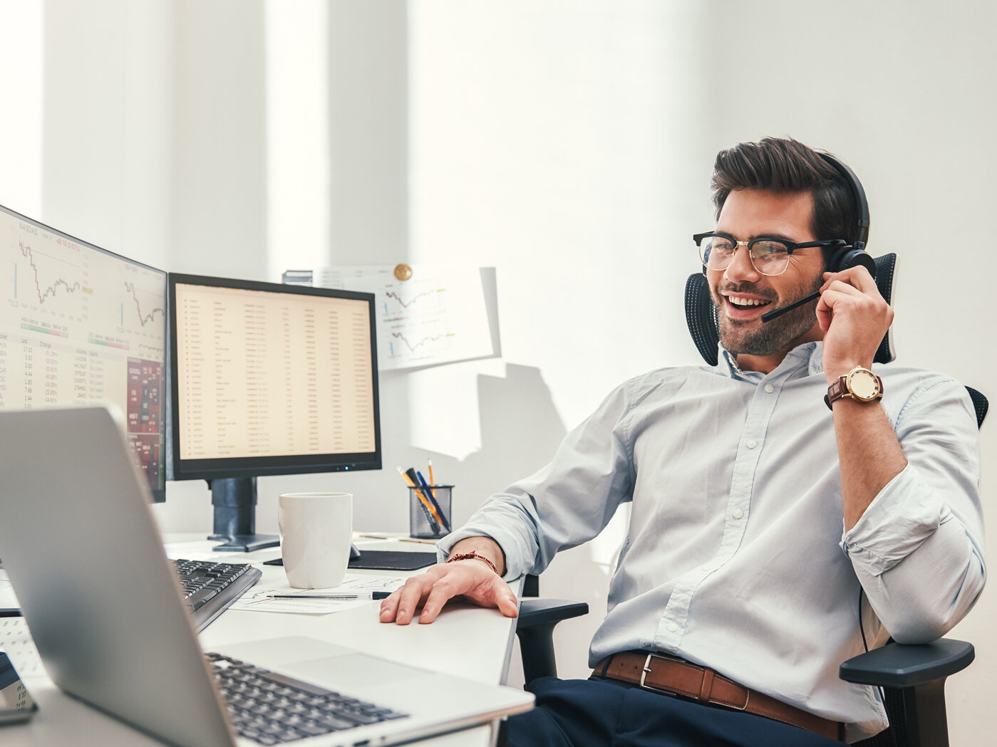 Ein Mann mit Brille und Bart telefoniert entspannt an einem Schreibtisch im Büro.