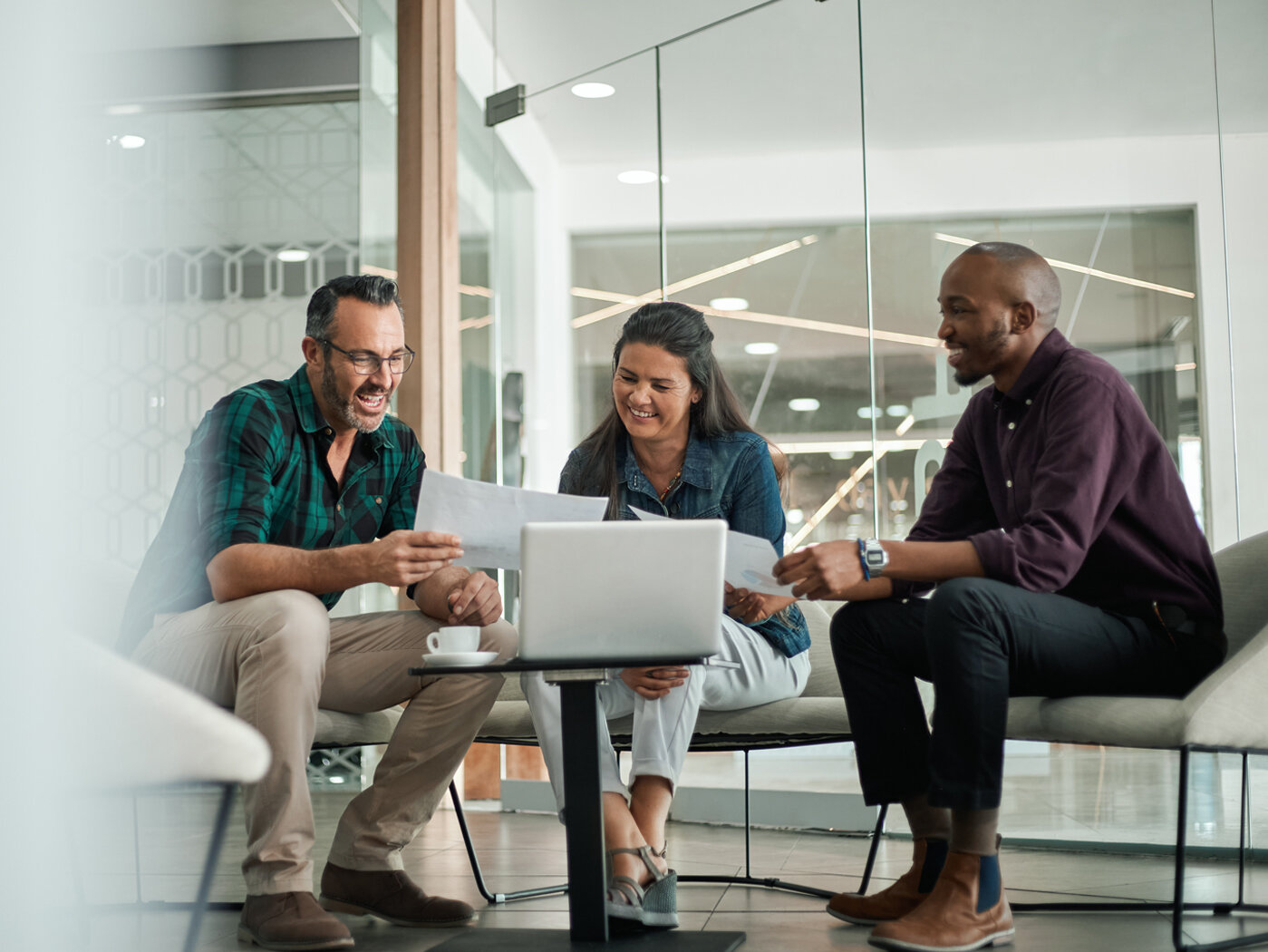 Drei Menschen sitzen in der Sitzecke eines modernen Büros und blicken auf einen Laptop.