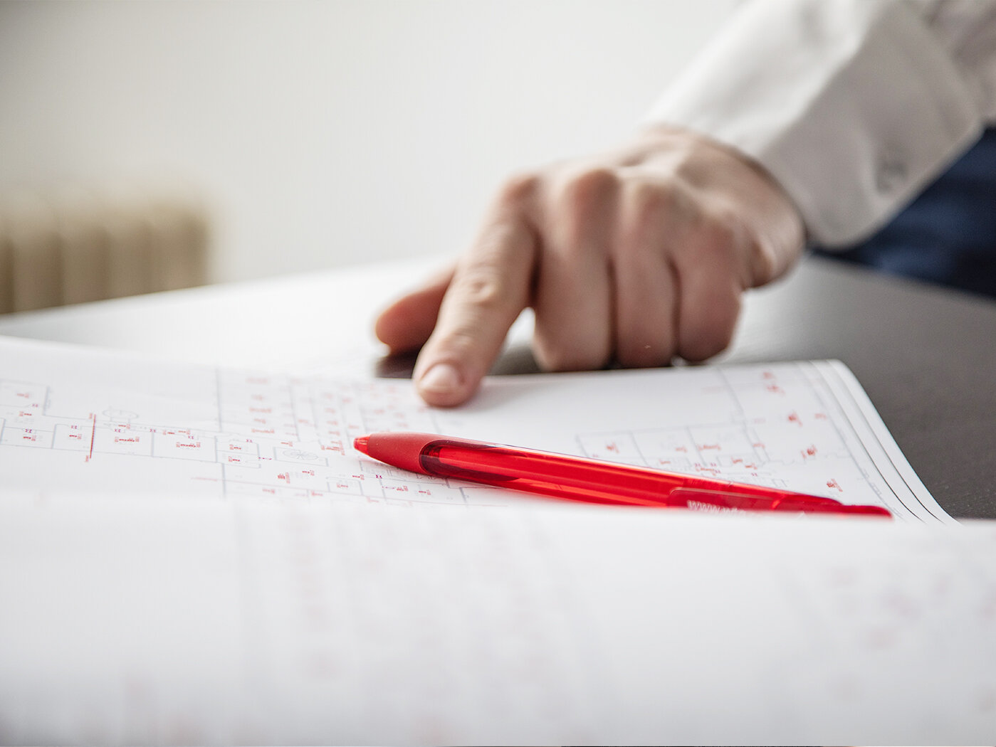Eine handschriftlich verfasste Gefährdungsanalyse liegt auf einem Tisch, daneben liegt ein roter Kuli und eine Hand weist auf den Text.
