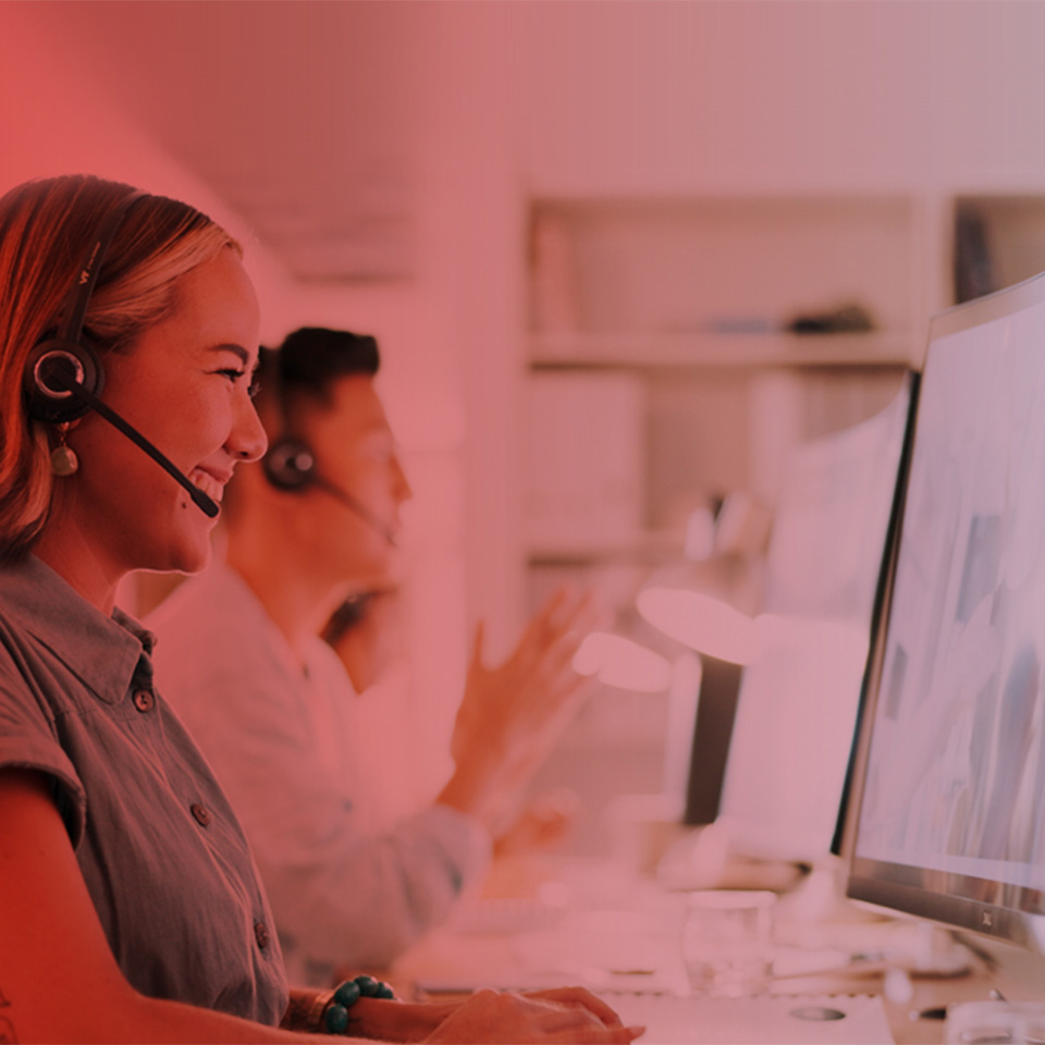 Eine freundliche Servicemitarbeiterin telefoniert am Computer und lächelt dabei.