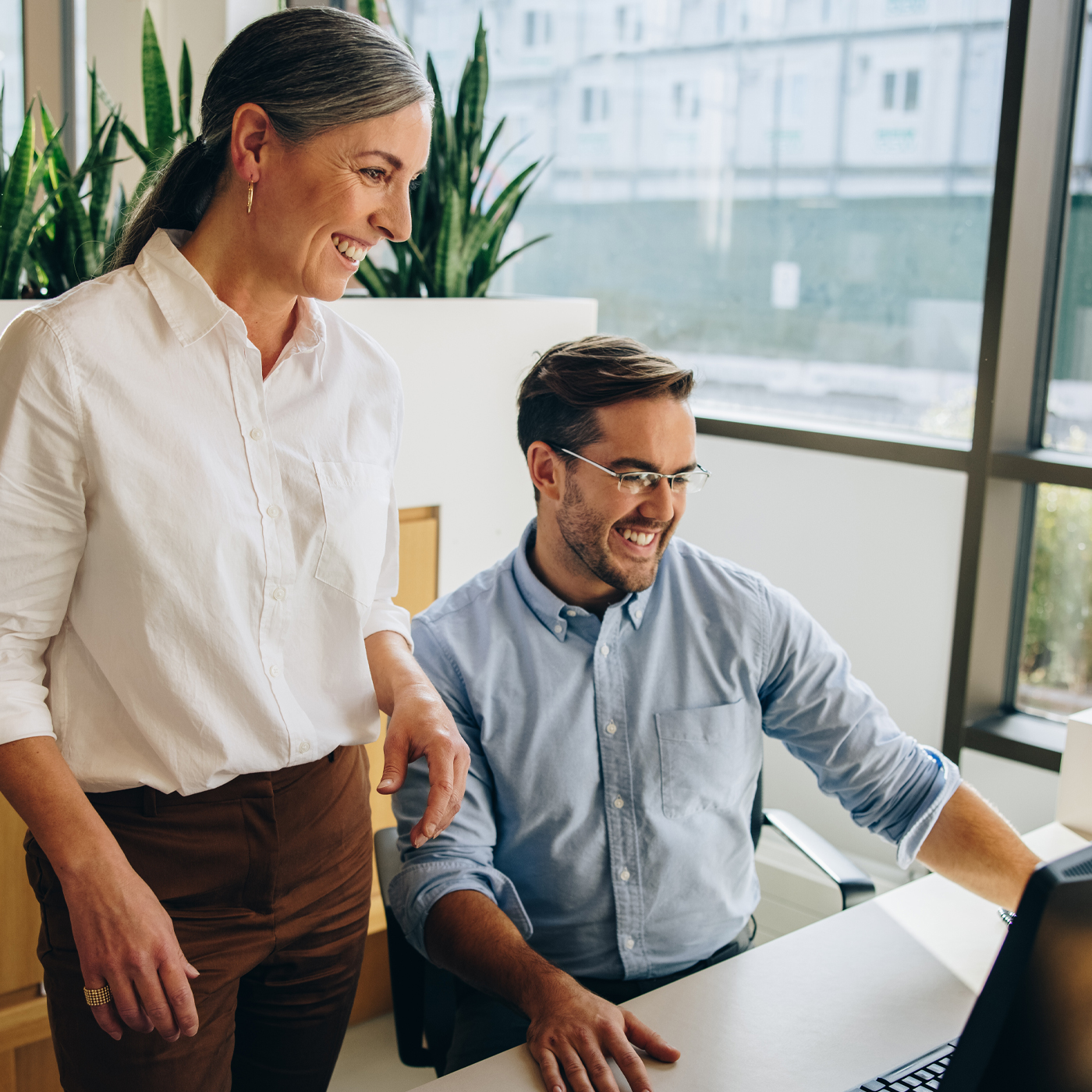 Ein Mann sitzt vor einem Computer; neben ihm steht eine Frau; beide lächseln.