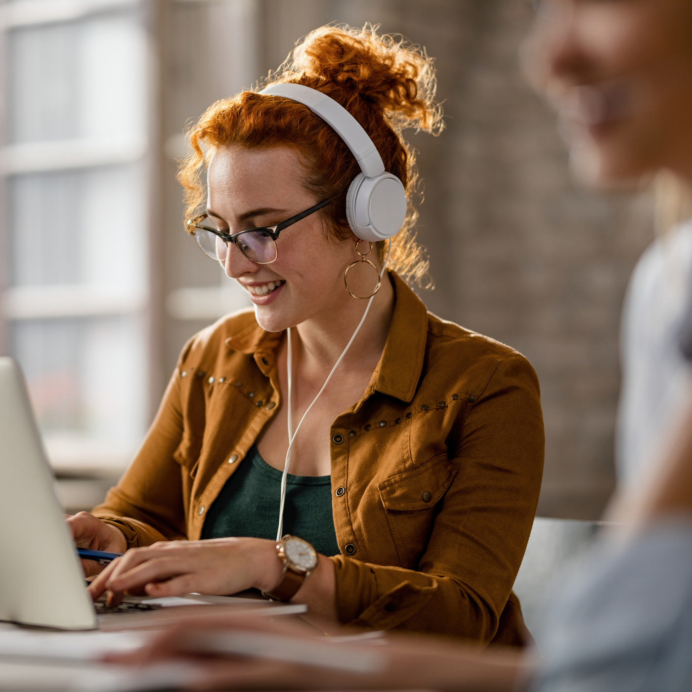 Eine rothaarige Frau mit einem Kopfhörer nutzt eine Public Cloud mit einem Laptop.